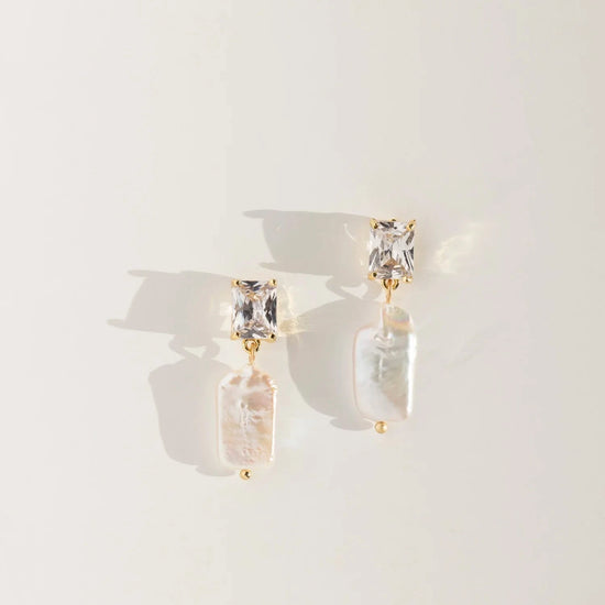 Pair of pearl earrings with clear stones on a light background