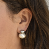 Close-up of an ear wearing a large, elegant pearl earring with a silver top. The earring contrasts against the skin and dark brown hair.