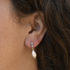 Close-up of an ear wearing a large, elegant pearl earring with a gold top. The earring contrasts against the skin and dark brown hair.
