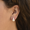 Close-up of an ear wearing elegant double pearl earrings. The larger pearl dangles below a smaller one, on a backdrop of brown hair.