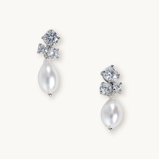 Silver stud earrings feature three sparkling diamonds and a dangling teardrop pearl. The elegant design conveys luxury and sophistication.