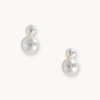 Elegant pearl earrings with two round, white pearls of varying sizes on each earring. They rest on a light background, conveying simplicity and sophistication.