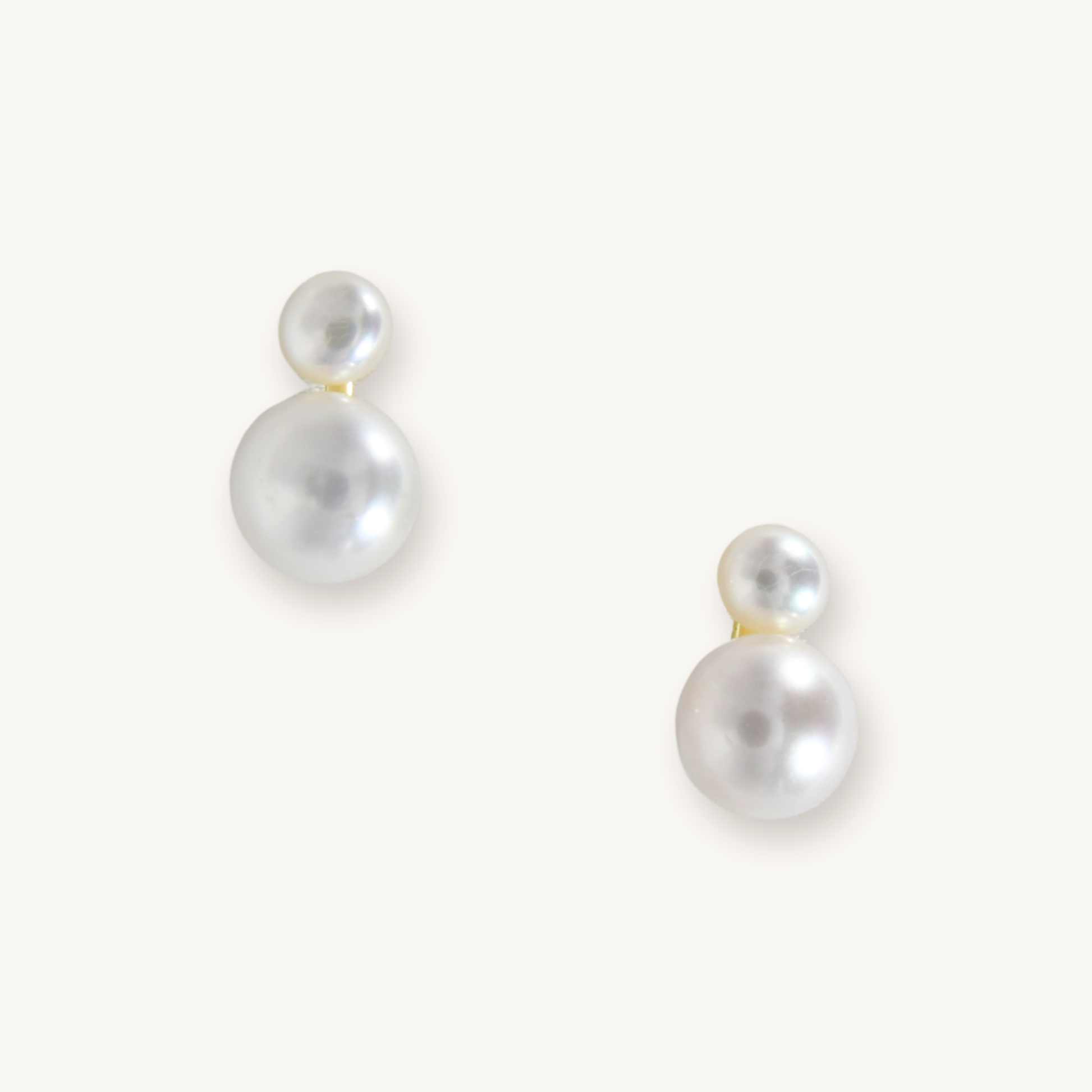 Elegant pearl earrings with two round, white pearls of varying sizes on each earring. They rest on a light background, conveying simplicity and sophistication.