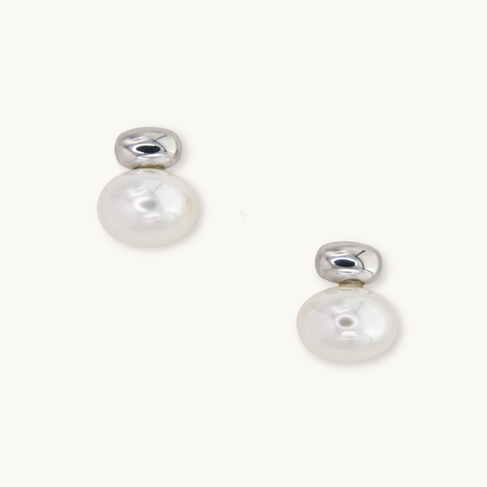 Silver earrings with round white pearls, reflecting light. Simple and elegant design on a plain white background, conveying a sense of sophistication.