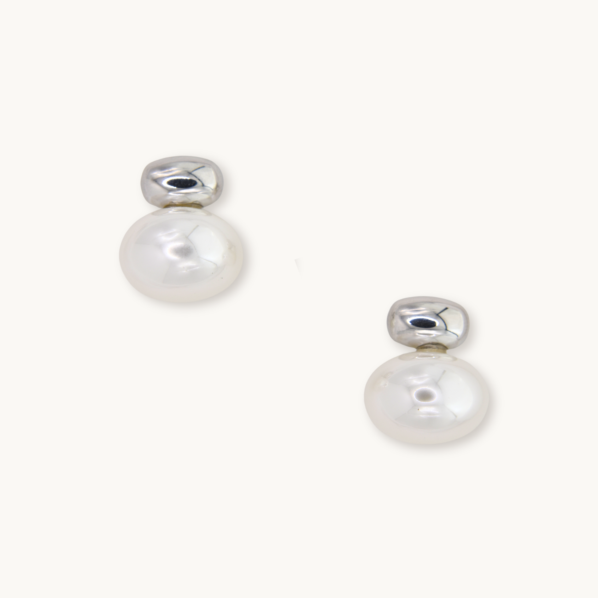Silver earrings with round white pearls, reflecting light. Simple and elegant design on a plain white background, conveying a sense of sophistication.