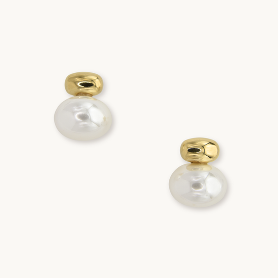 Gold earrings with round white pearls, reflecting light. Simple and elegant design on a plain white background, conveying a sense of sophistication.