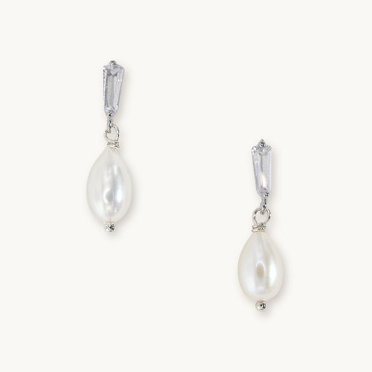 Elegant silver earrings featuring teardrop-shaped pearls with shiny rectangular stone studs. Minimalist and sophisticated design on a plain background.