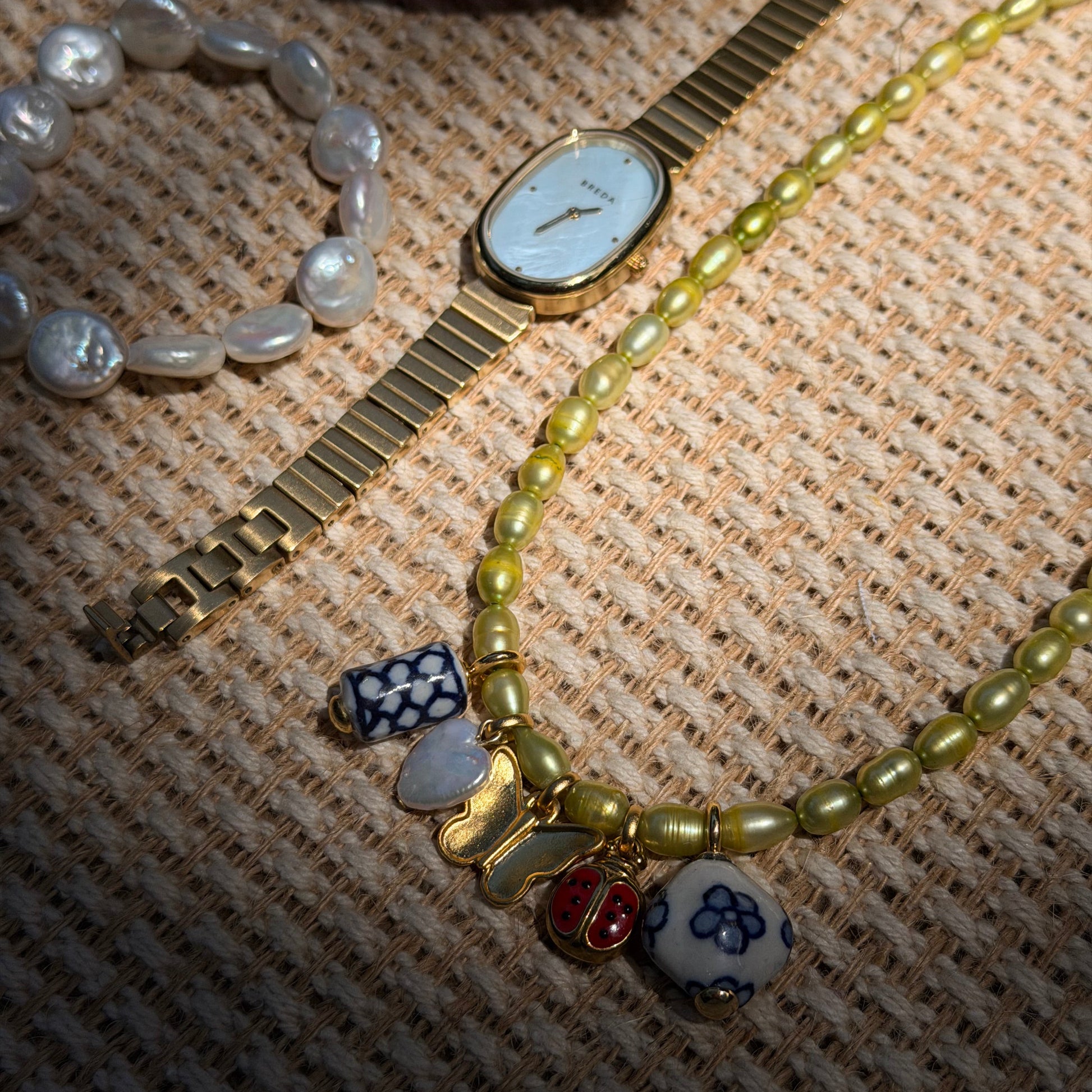 Gold watch and beaded bracelet with charms on a textured fabric background