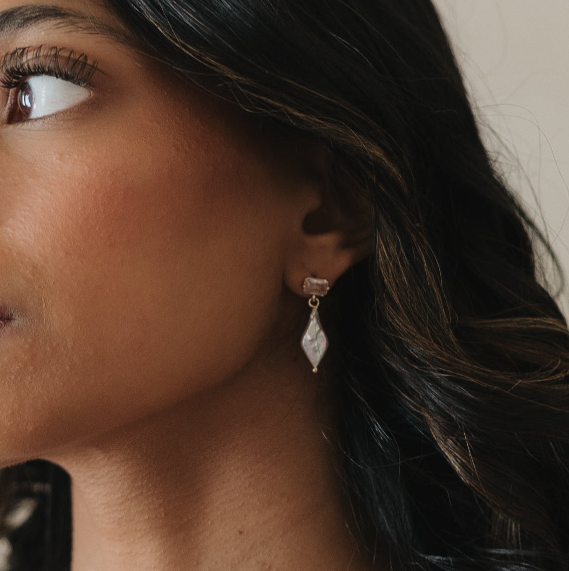 Close-up of a woman wearing a diamond earring with a neutral background