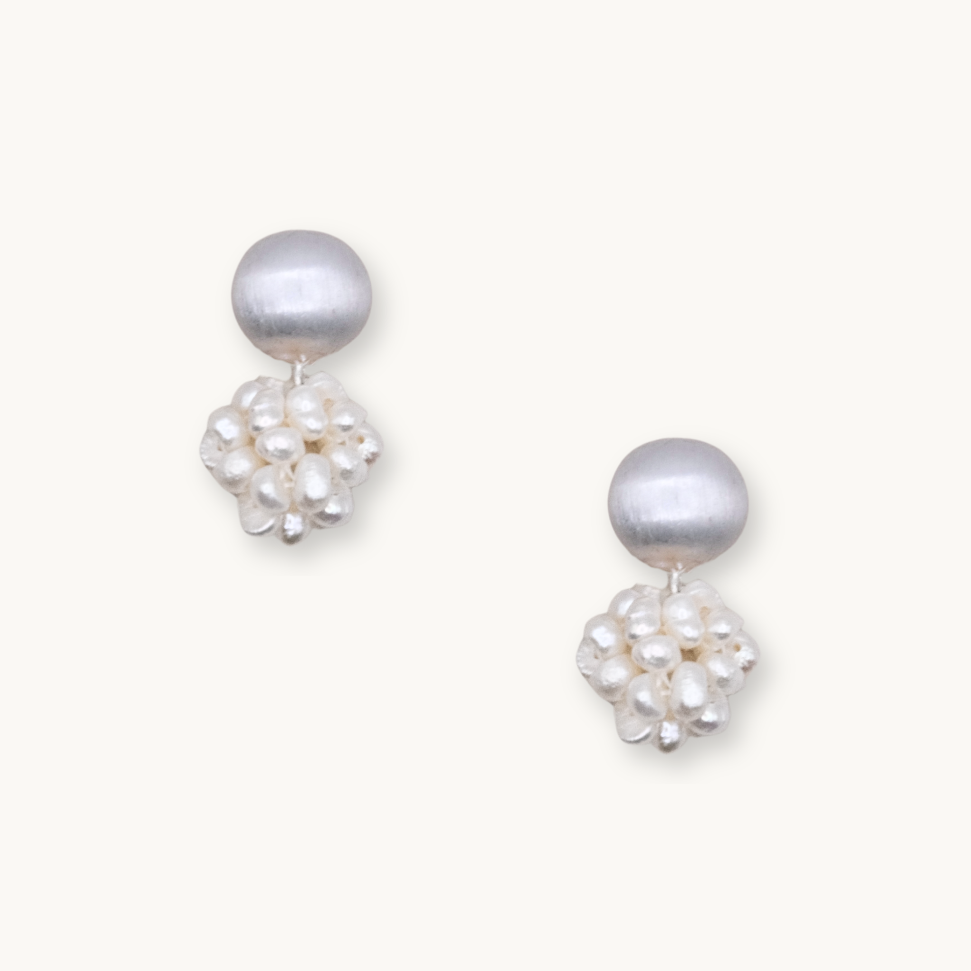 Elegant pearl earrings featuring a smooth, round white pearl atop a cluster of smaller, irregular pearls on a light background.