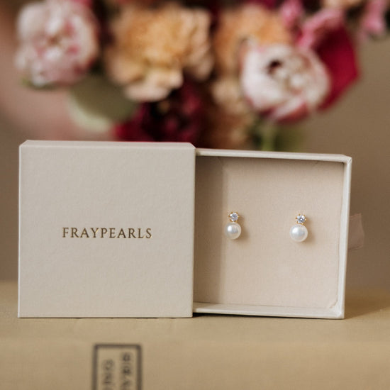 Pearl earrings in a 'Fraypearls' box with flowers in the background