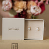 Pearl earrings in a 'Fraypearls' box with flowers in the background