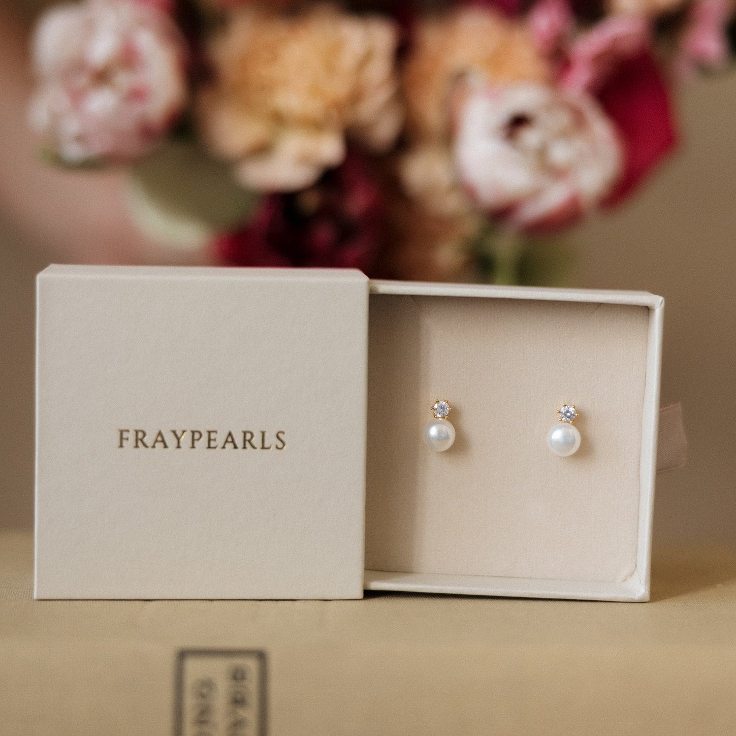 Pearl earrings in a 'Fraypearls' box with flowers in the background