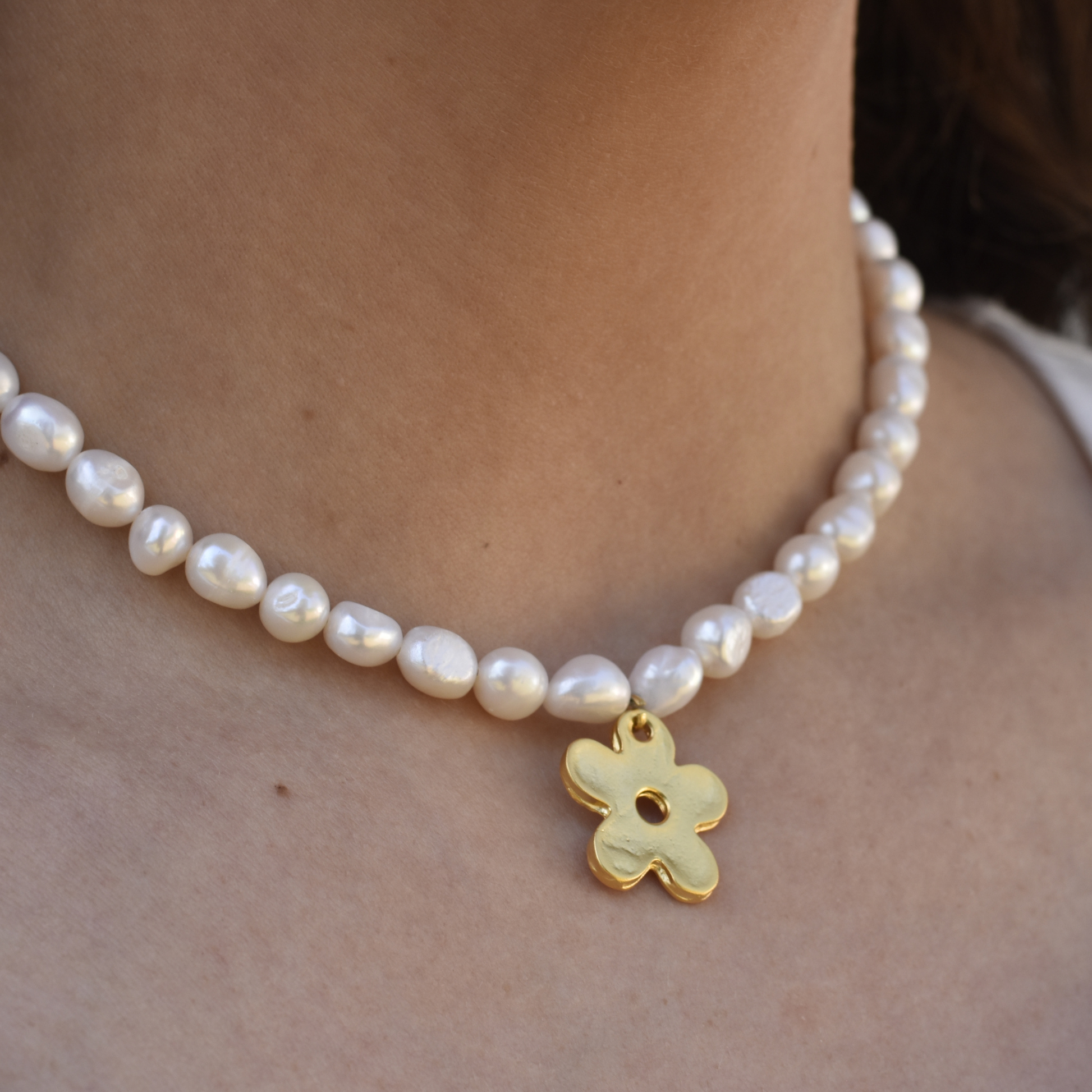 A necklace of irregular white pearls encircles a neck, featuring a gold flower-shaped charm. The tone is elegant and classic.