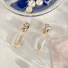 Pair of earrings with clear stones and gold accents on a white surface with a blue and white patterned dish in the background.