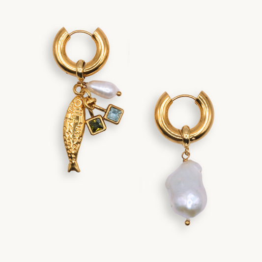 Two mismatched gold hoop earrings: one with charms including a fish, pearl, and gemstones, the other with a single large baroque pearl, conveying elegance and whimsy.