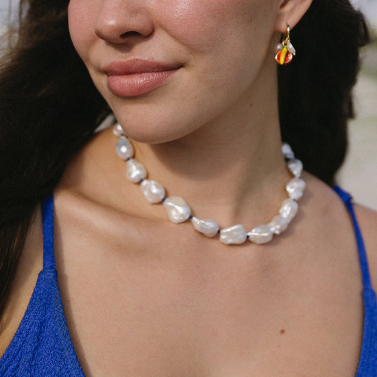 Close-up of a woman wearing a pearl necklace and colorful earrings.