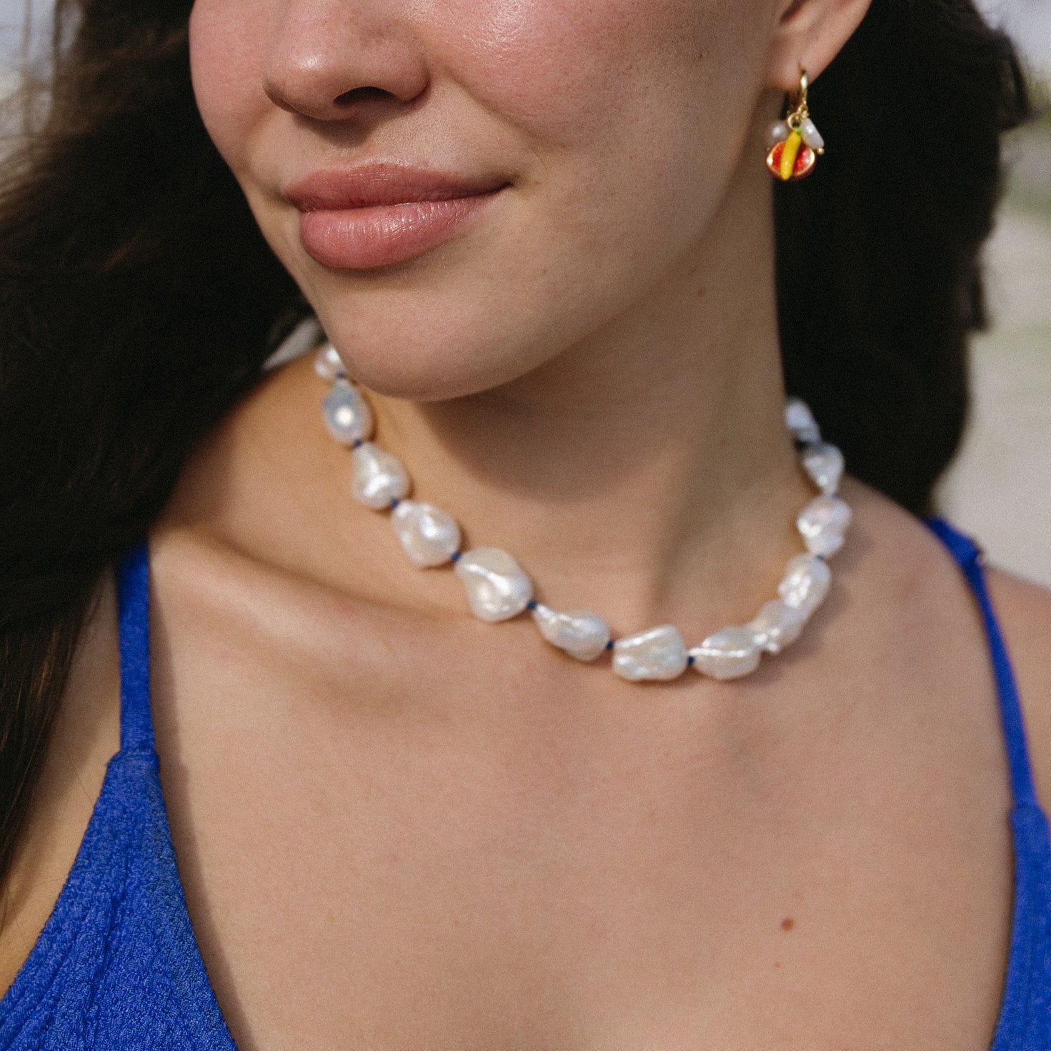 Close-up of a woman wearing a pearl necklace and colorful earrings.