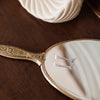 Decorative hand mirror with intricate gold handle on a wooden surface