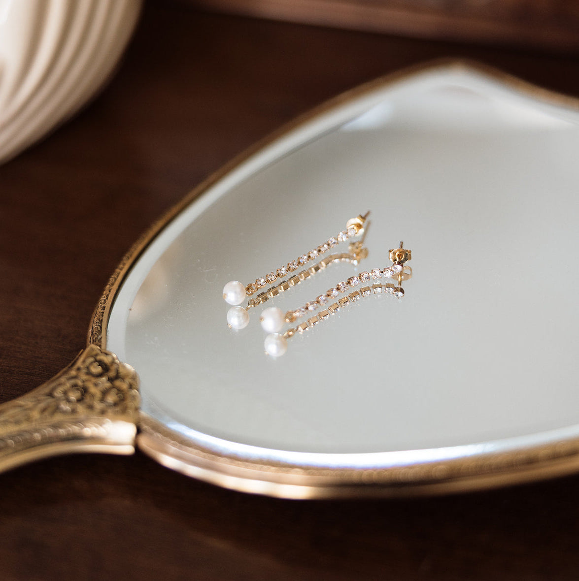 Pearl earrings on a decorative hand mirror with a wooden background