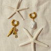 Gold and pearl earrings with starfish on a beige fabric background