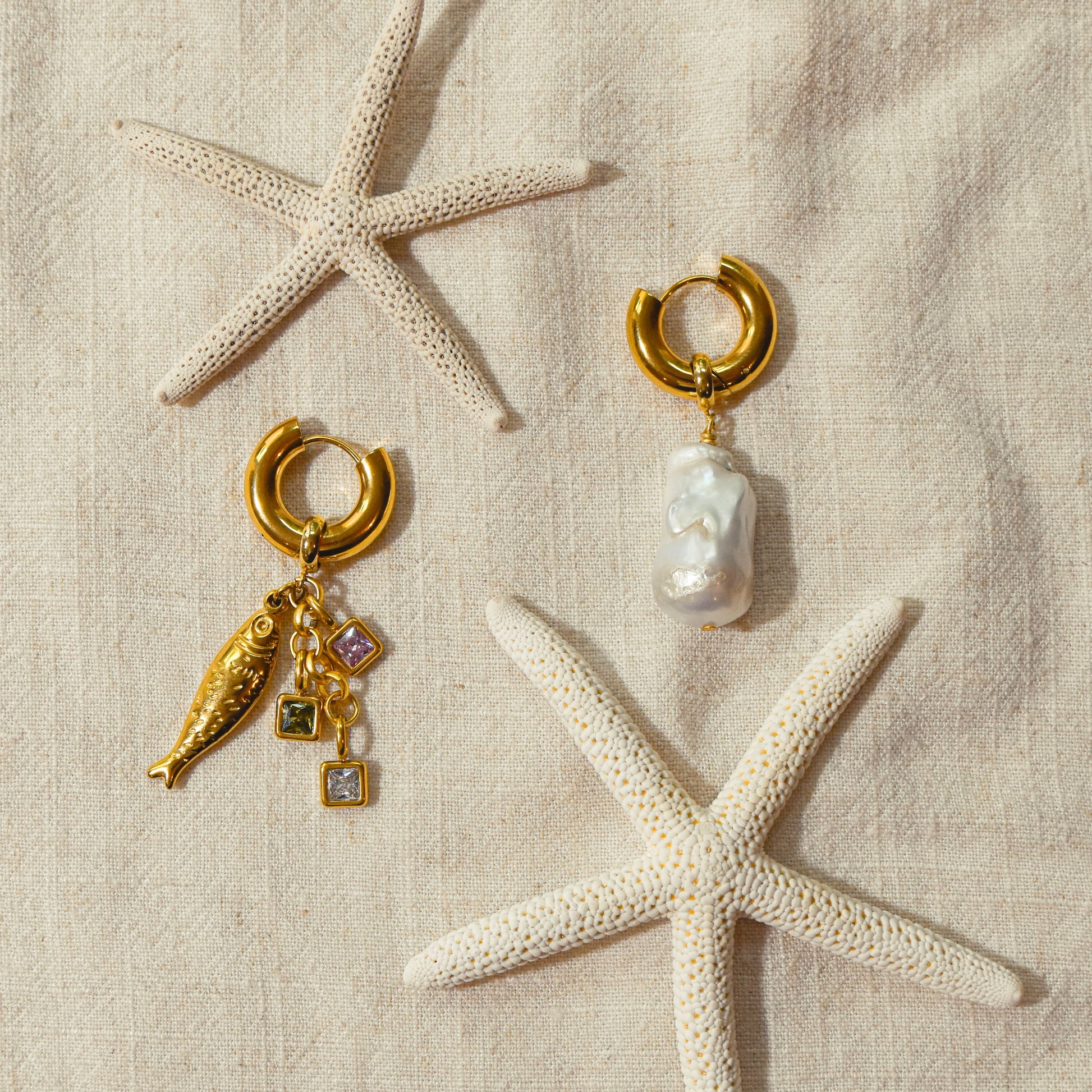 Gold and pearl earrings with starfish on a beige fabric background