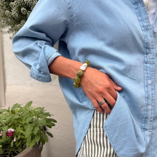 Person wearing a blue shirt and striped pants with a green bracelet, standing next to a plant.
