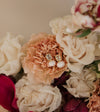 Elegant pearl and gold earrings rest on a peach carnation, surrounded by white and red roses, creating a soft, romantic atmosphere.