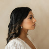 Woman wearing a white textured top against a beige background with bridal pearl earrings conveying timeless and natural bridal beauty. 