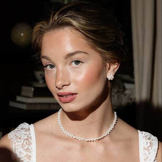 A woman in elegant attire holds a vintage hand mirror. She wears a pearl necklace and lace dress, conveying a classic and sophisticated look.