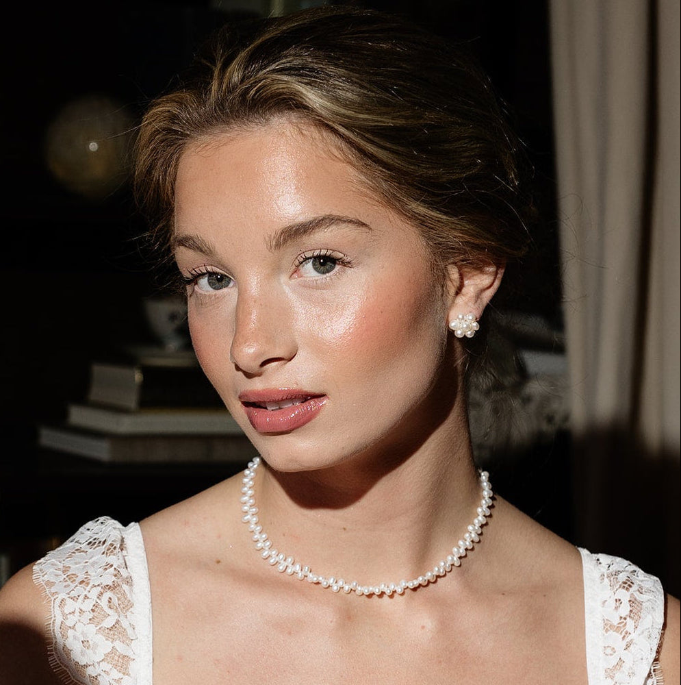 A woman in elegant attire holds a vintage hand mirror. She wears a pearl necklace and lace dress, conveying a classic and sophisticated look.