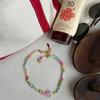 Colorful pearl bracelet beside a red-trimmed bag, SPF 30 sunscreen with a hibiscus, sunglasses, and brown sandals, evoking a relaxed beach vibe.