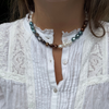 A close-up of a person wearing a pearl necklace with white, teal, and brown over a white lace blouse.