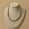 A strand of irregular freshwater pearl necklace in soft pastel colors, displayed on a beige fabric jewelry bust against a warm beige background.