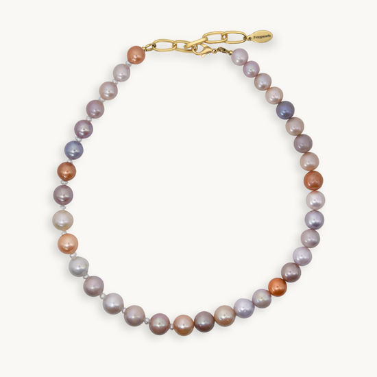 A necklace made of freshwater pearls in shades of lavender, gray, peach, and bronze, finished with a gold clasp and extender chain.