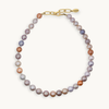 A necklace made of freshwater pearls in shades of lavender, gray, peach, and bronze, finished with a gold clasp and extender chain.
