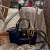 A navy blue handbag with gold hardware and the brand name 'fraypearls' embroidered on the front, resting on a brown and beige plaid blanket draped over a wicker chair in an outdoor cafe setting.