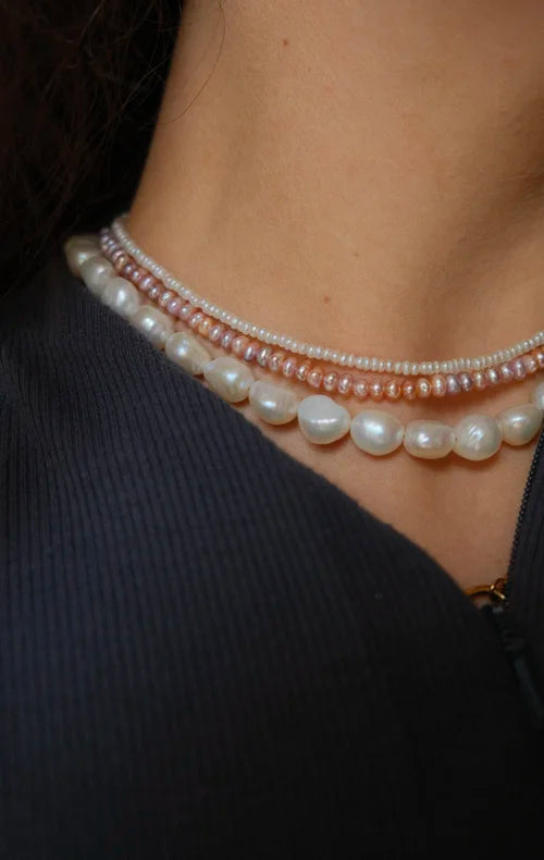 Close-up of a person wearing multiple pearl necklaces against a dark background