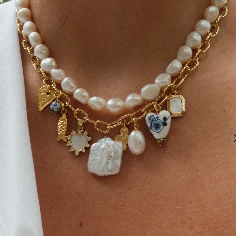 Necklace with pearls and various charms on a person wearing a white shirt.