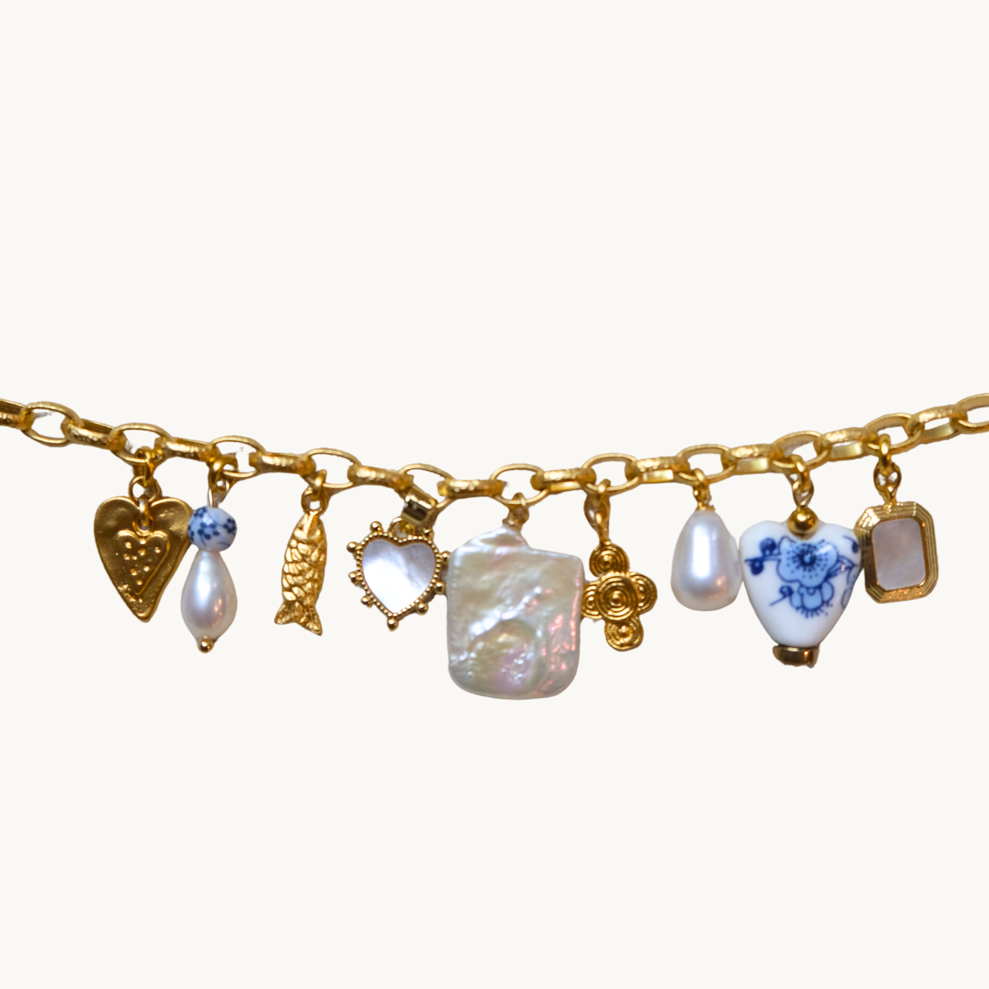 A gold charm bracelet featuring multiple dangling charms, including heart-shaped mother-of-pearl pendants with blue floral details, a large irregular white pearl, a gold rose charm, and a small rectangular white stone charm, displayed against a solid off-white background.