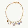 A gold chain necklace with multiple dangling charms, including a blue and white patterned vase, a white pearl, a gold heart, and other small decorative charms, displayed on a clean off-white background.