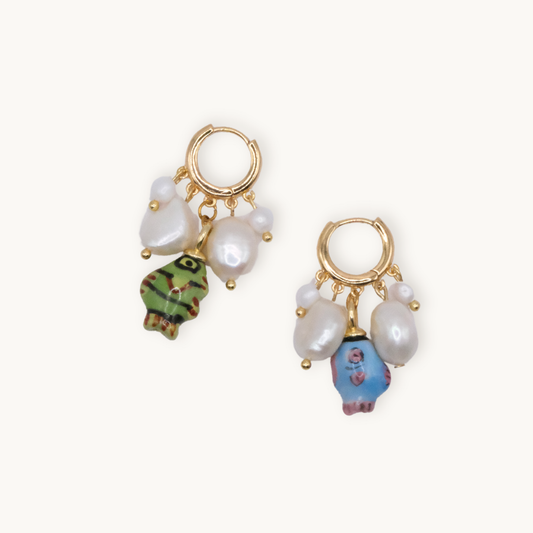 Gold hoop earrings adorned with white pearls and colorful fish-shaped pendants, one green and one blue. The design is playful and artistic.