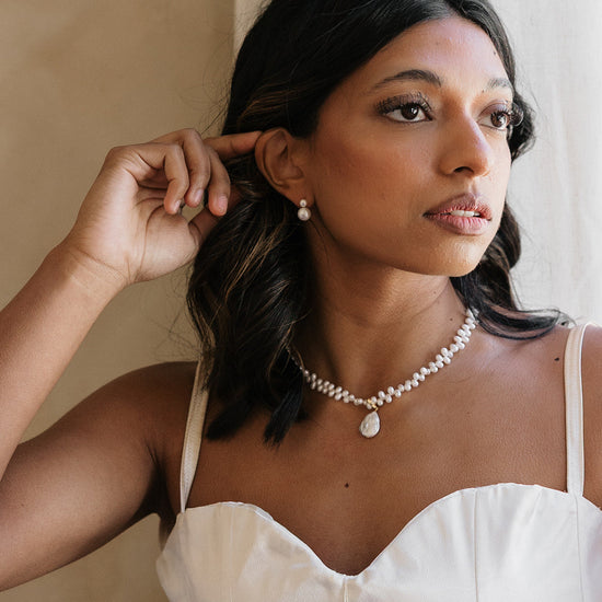 Woman wearing a pearl necklace and earrings indoors with neutral background