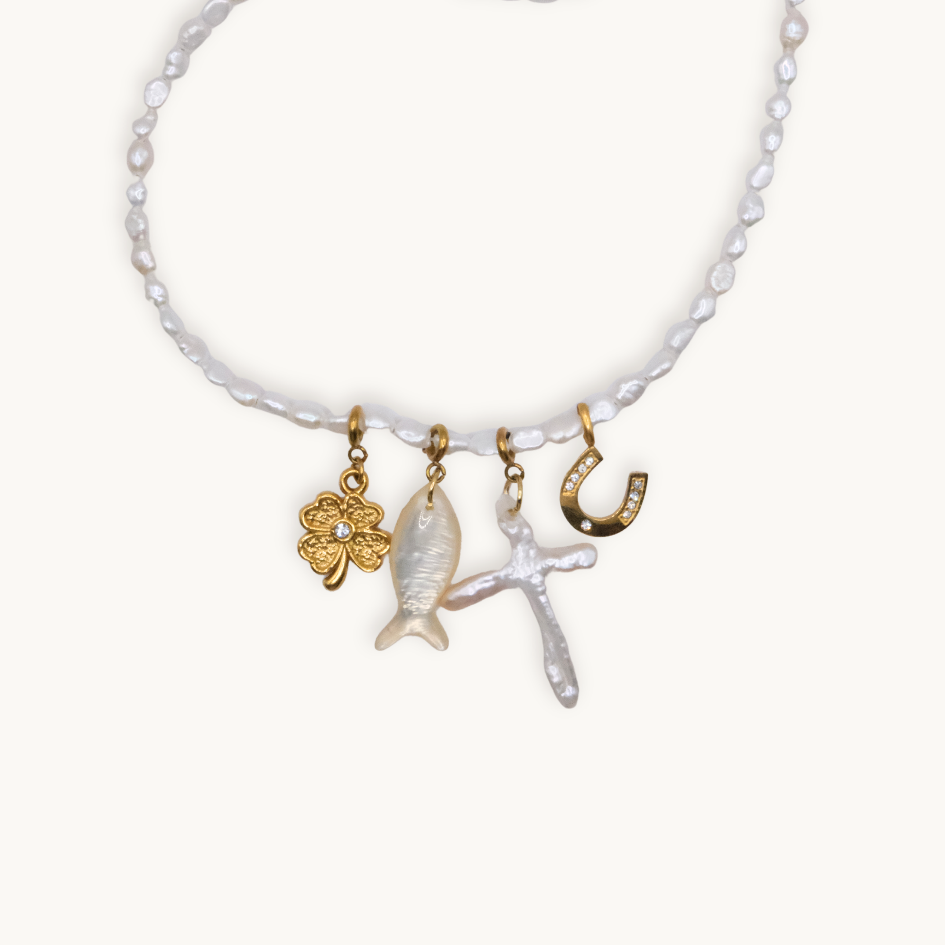 A wrap necklace of white irregular pearls featuring four charms: a gold clover, a fish, a cross, and a horseshoe, each with intricate details.