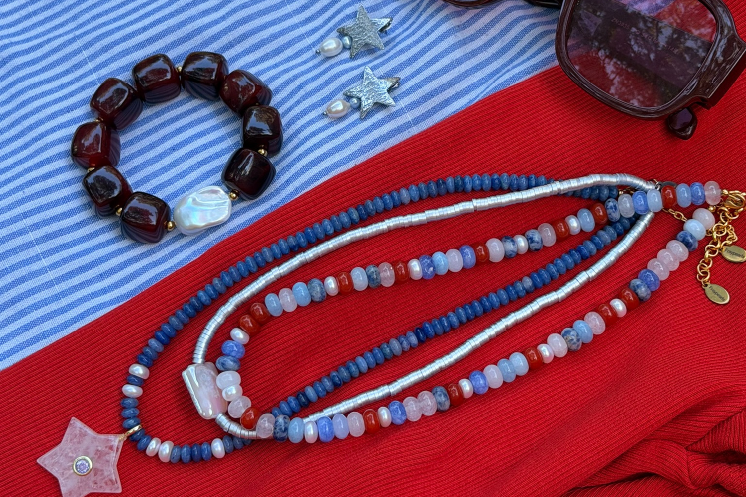 Jewelry including a bracelet, necklace, and earrings on a red and blue striped fabric background.