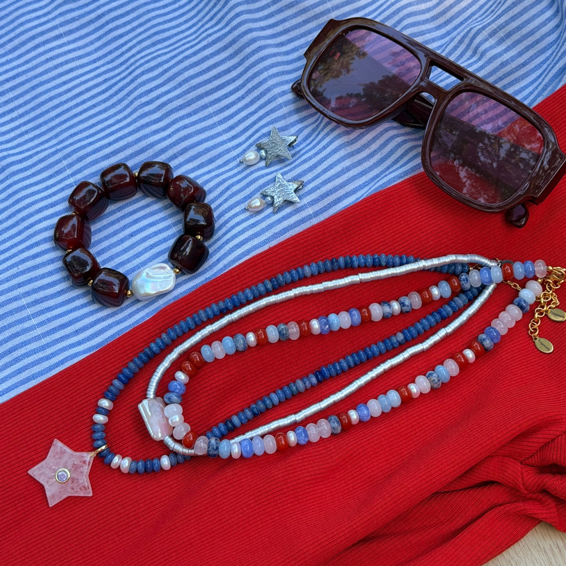 Jewelry including a bracelet, necklace, and earrings on a red and blue striped fabric background.