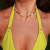 A colorful necklace with red, green, and white pearls, including a flower-shaped bead, around a person's neck wearing a bright green bikini top.