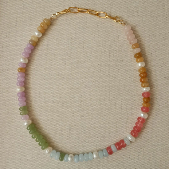 Necklace with multicolored beads and pearls on a beige fabric background