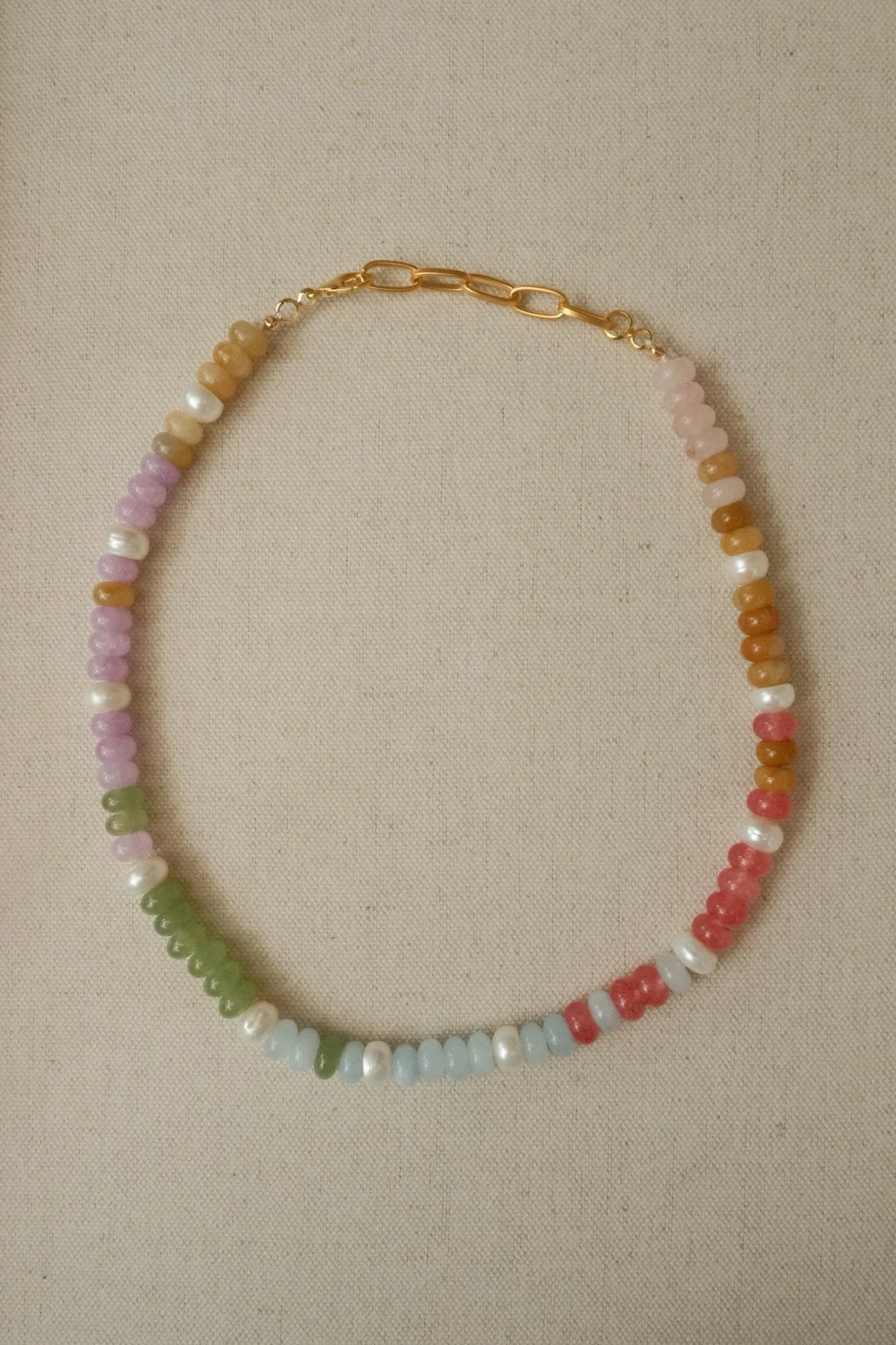 Necklace with multicolored beads and pearls on a beige fabric background