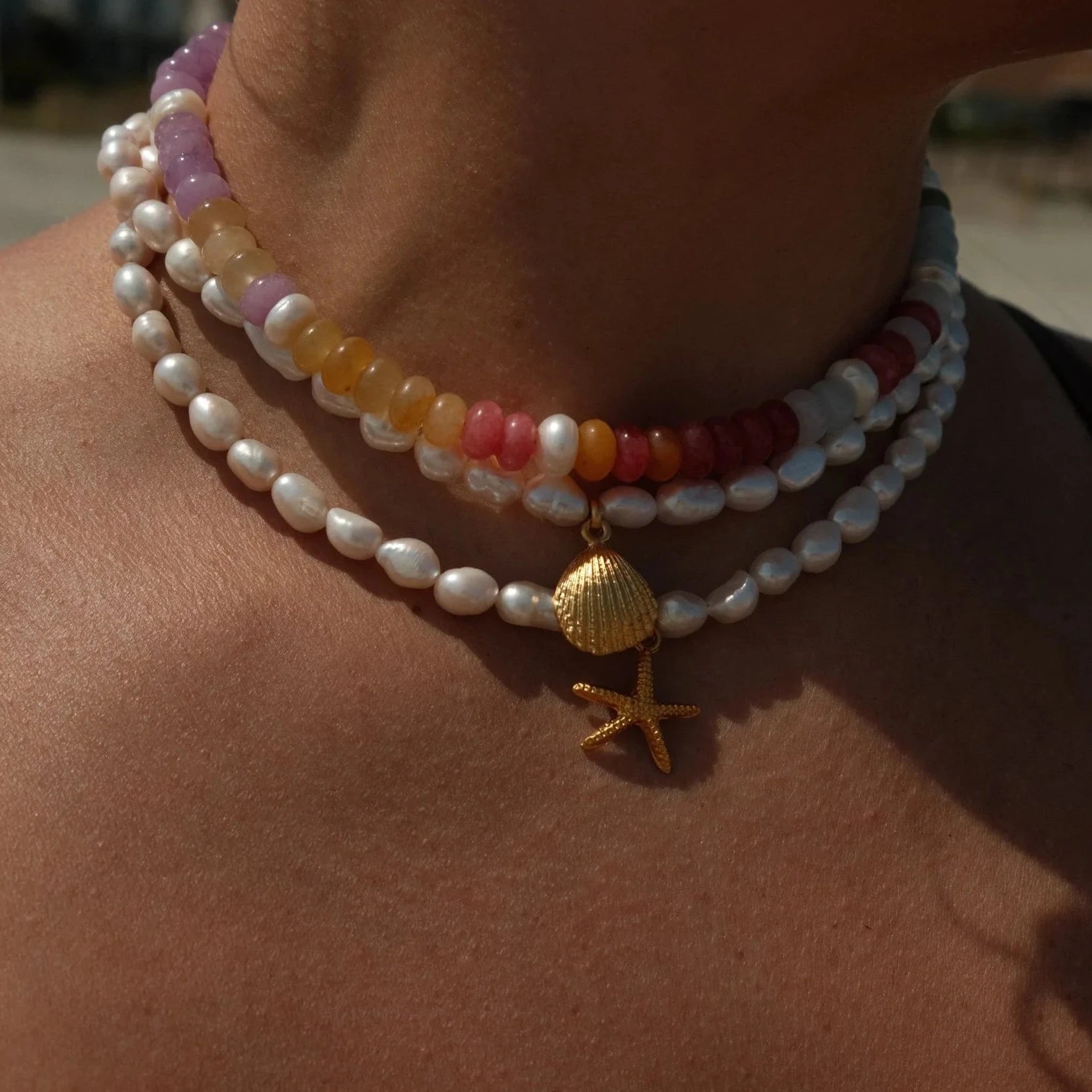 Close-up of a person wearing multiple necklaces with shell and starfish charms.